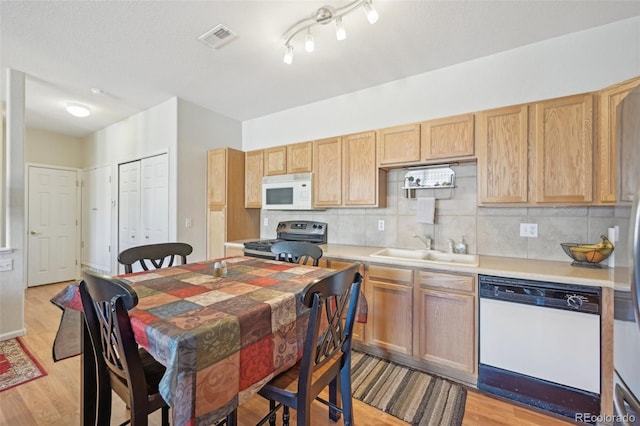 kitchen with backsplash, light hardwood / wood-style floors, rail lighting, sink, and white appliances