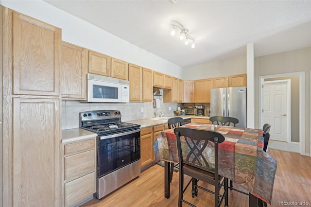 kitchen with light brown cabinets, backsplash, track lighting, light hardwood / wood-style floors, and stainless steel appliances