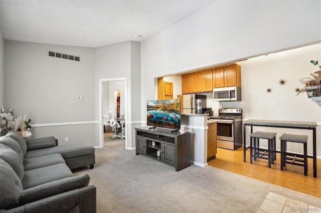 living area featuring a textured ceiling, high vaulted ceiling, light carpet, visible vents, and baseboards