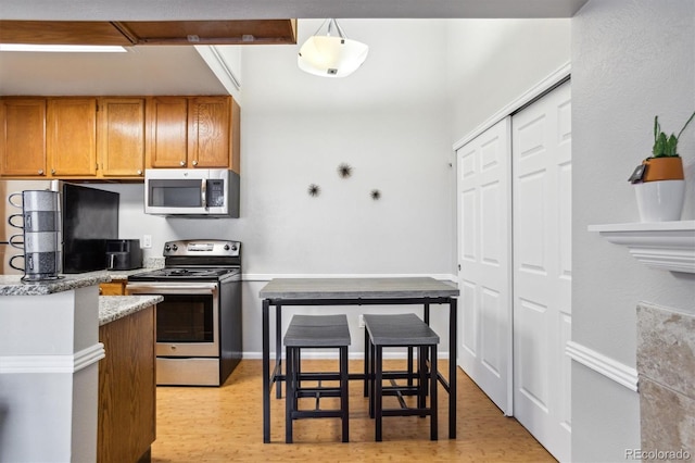 kitchen with brown cabinets, light wood finished floors, stainless steel appliances, hanging light fixtures, and baseboards