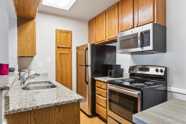 kitchen featuring appliances with stainless steel finishes, brown cabinetry, a sink, and light stone countertops