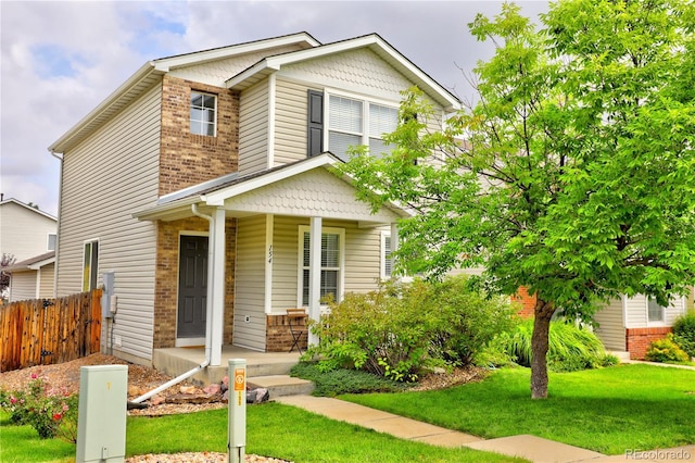 view of front of property with a front yard, covered porch, brick siding, and fence