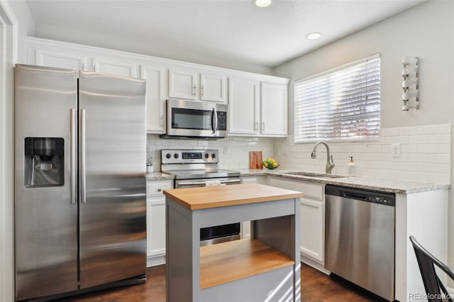 kitchen with white cabinets, butcher block countertops, appliances with stainless steel finishes, a sink, and backsplash