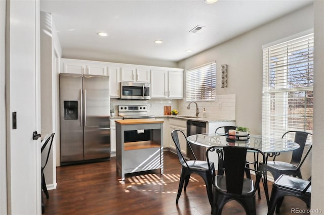 kitchen with stainless steel appliances, decorative backsplash, a sink, and white cabinets