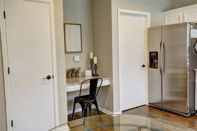 kitchen with dark wood-style flooring, white cabinets, stainless steel refrigerator with ice dispenser, built in study area, and light stone countertops