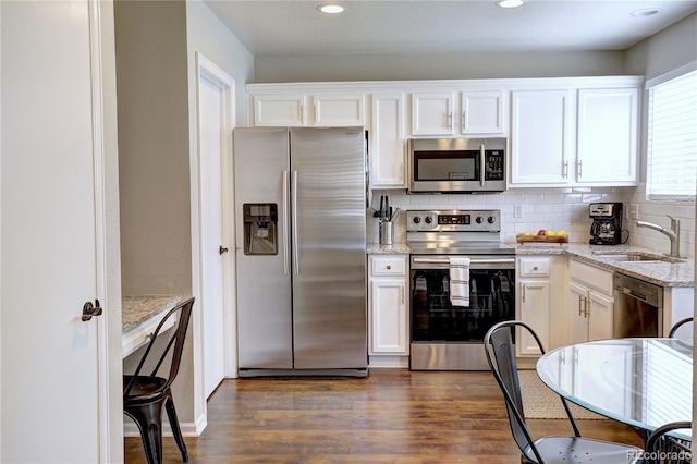 kitchen with appliances with stainless steel finishes, dark wood-style flooring, a sink, white cabinetry, and backsplash