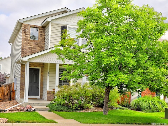 view of front of house featuring covered porch, brick siding, fence, and a front lawn