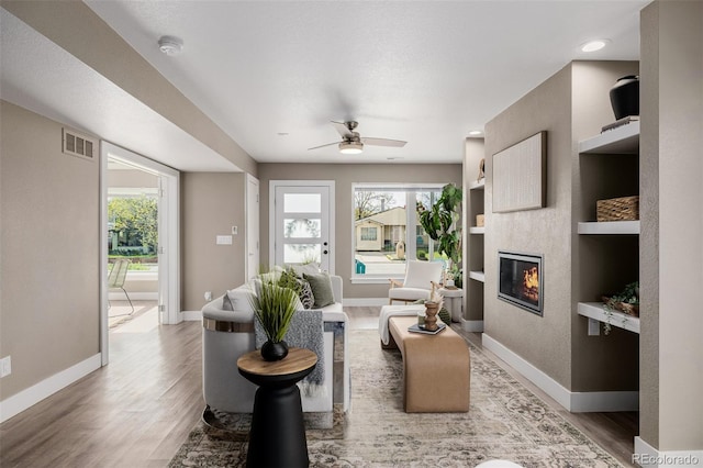 living room featuring baseboards, light wood-style flooring, a glass covered fireplace, and ceiling fan