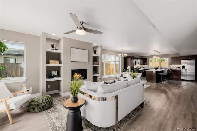 living area featuring a chandelier, wood finished floors, plenty of natural light, and a glass covered fireplace