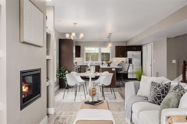 living area with light wood-type flooring, a chandelier, a glass covered fireplace, and baseboards