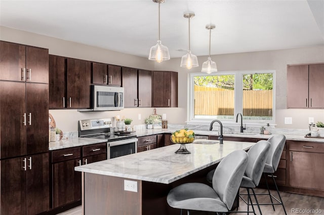 kitchen featuring appliances with stainless steel finishes, a kitchen breakfast bar, a sink, a kitchen island, and wood finished floors