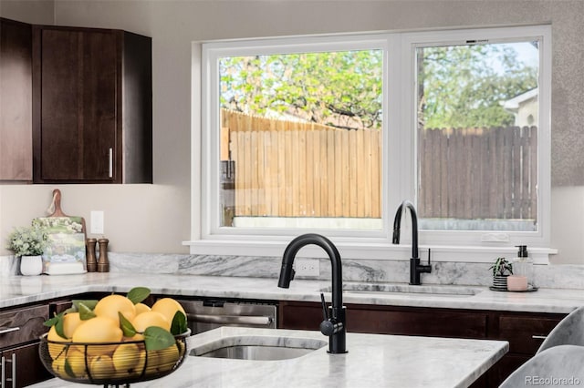 kitchen featuring dark brown cabinetry, light stone counters, and a sink