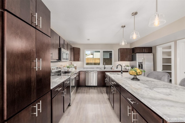 kitchen with appliances with stainless steel finishes, light wood-style floors, a sink, dark brown cabinetry, and hanging light fixtures