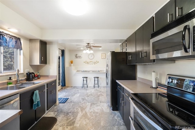 kitchen featuring a ceiling fan, appliances with stainless steel finishes, light countertops, dark cabinetry, and a sink