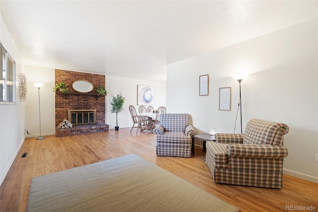 living room featuring a brick fireplace, wood finished floors, visible vents, and baseboards