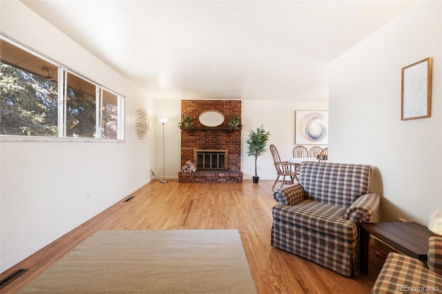 living area featuring a brick fireplace, visible vents, baseboards, and wood finished floors