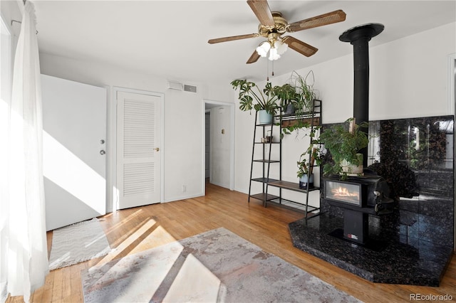 interior space with a wood stove, wood-type flooring, and ceiling fan