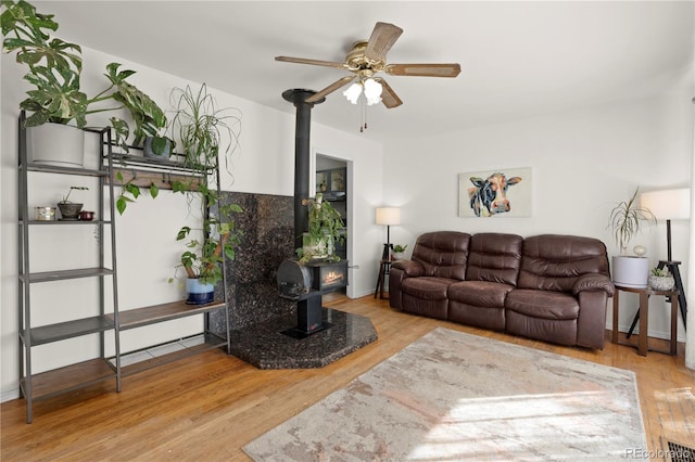 living room featuring a wood stove, light hardwood / wood-style floors, and ceiling fan