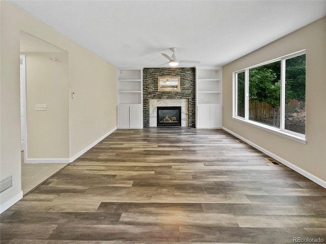 unfurnished living room with ceiling fan, a large fireplace, wood-type flooring, and built in shelves