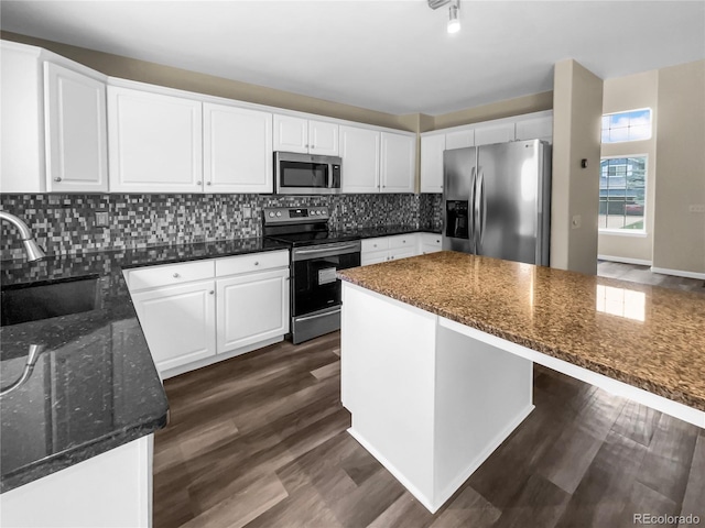 kitchen with sink, white cabinetry, stainless steel appliances, a kitchen island, and dark stone counters