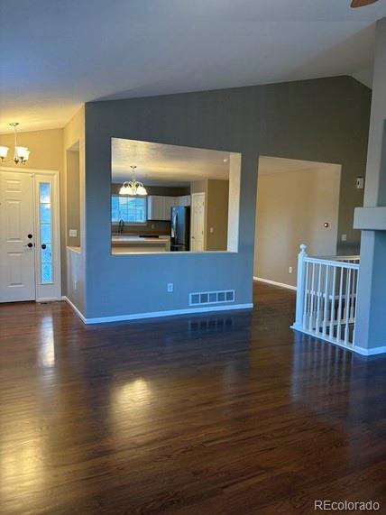 unfurnished living room with dark wood-style floors, vaulted ceiling, and an inviting chandelier