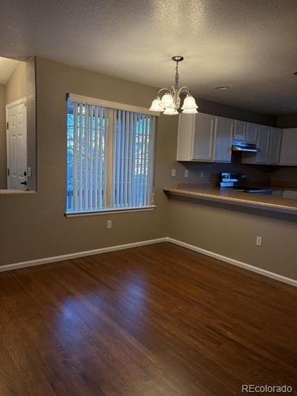 kitchen featuring under cabinet range hood, dark wood-type flooring, stove, baseboards, and decorative light fixtures