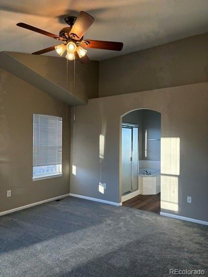 unfurnished room with baseboards, arched walkways, a ceiling fan, lofted ceiling, and dark colored carpet