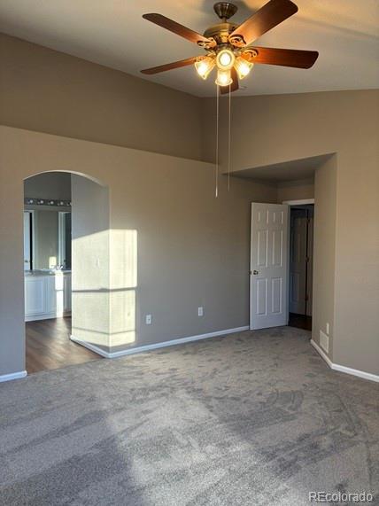 empty room featuring arched walkways, lofted ceiling, carpet flooring, a ceiling fan, and baseboards