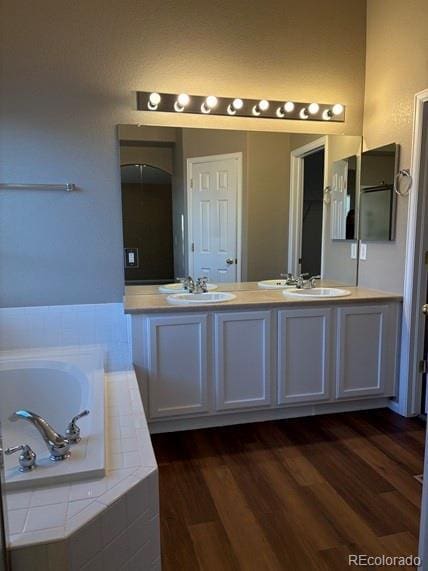 full bath featuring double vanity, a garden tub, a sink, and wood finished floors