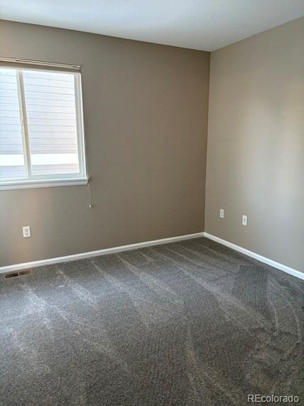 empty room with baseboards, visible vents, and dark colored carpet