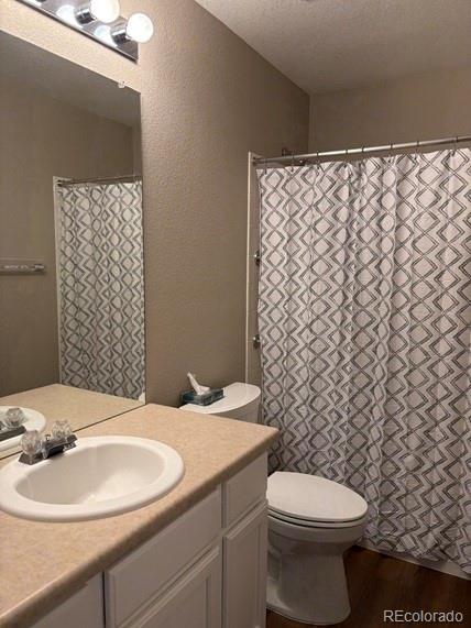 bathroom featuring a textured ceiling, a textured wall, toilet, wood finished floors, and vanity