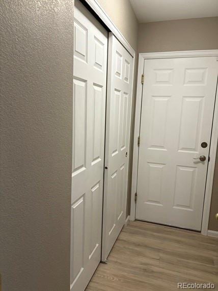 hall featuring light wood finished floors and a textured wall