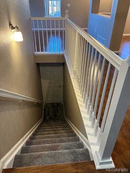 stairs with a textured wall, wood finished floors, visible vents, and baseboards