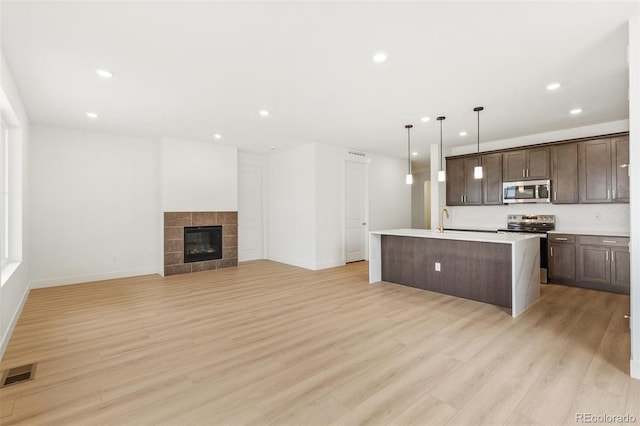 20665 E 57th Dr, Aurora, CO 80019 - kitchen featuring stainless steel appliances, a sink, dark brown cabinets, baseboards, and a kitchen island with sink