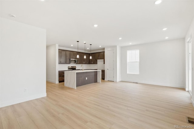 20665 E 57th Dr, Aurora, CO 80019 - kitchen with stainless steel appliances, dark brown cabinets, light countertops, light wood-style flooring, and a center island with sink