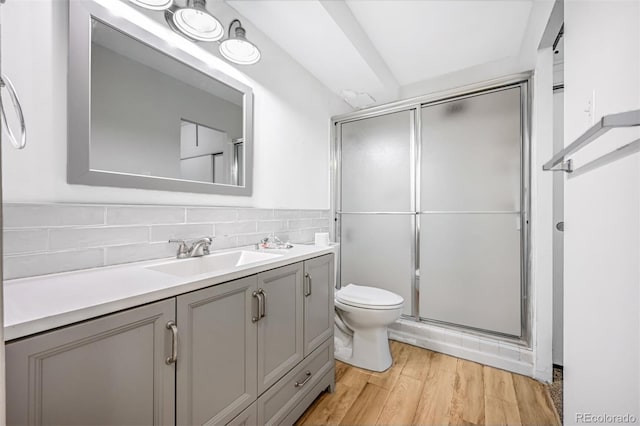 bathroom with decorative backsplash, hardwood / wood-style flooring, toilet, vanity, and walk in shower