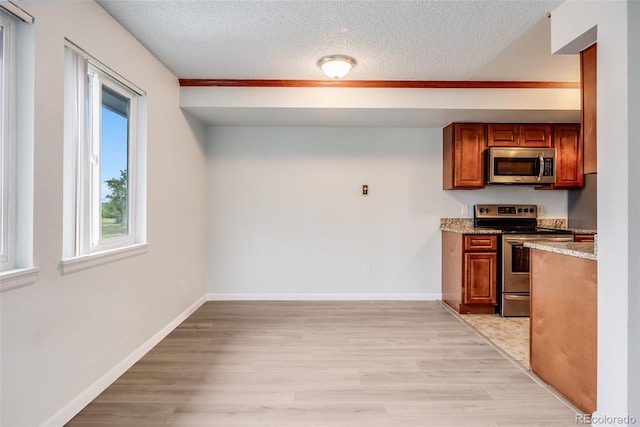 kitchen with a textured ceiling, light stone counters, light wood-type flooring, and stainless steel appliances