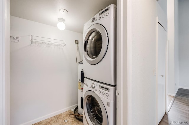 laundry room with laundry area, electric water heater, stacked washer / drying machine, and baseboards