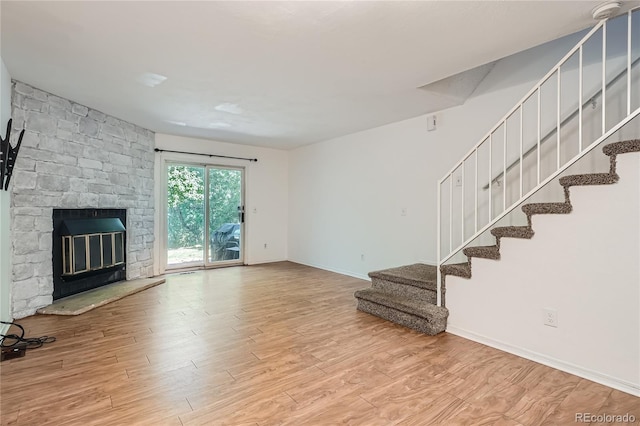 unfurnished living room featuring wood-type flooring and a stone fireplace