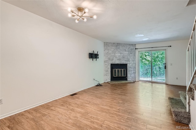 unfurnished living room featuring a stone fireplace, light hardwood / wood-style floors, and a chandelier