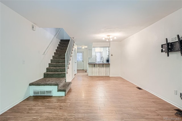 staircase featuring wood-type flooring, a notable chandelier, and sink