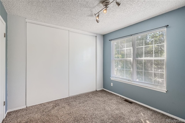 spare room featuring a textured ceiling, rail lighting, and carpet flooring