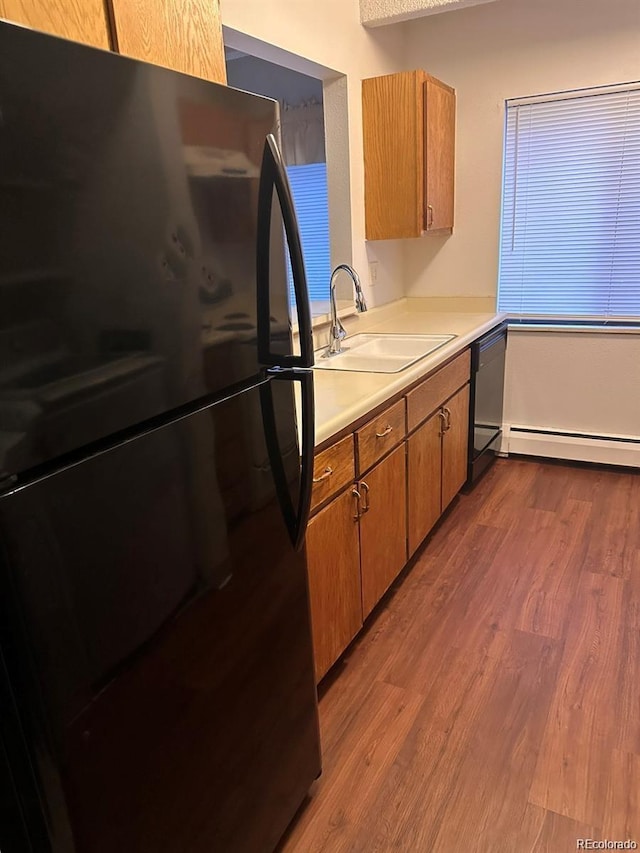 kitchen featuring dark wood-style flooring, brown cabinets, light countertops, a sink, and black appliances