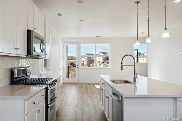 kitchen featuring white cabinets, decorative light fixtures, stainless steel appliances, and a kitchen island with sink