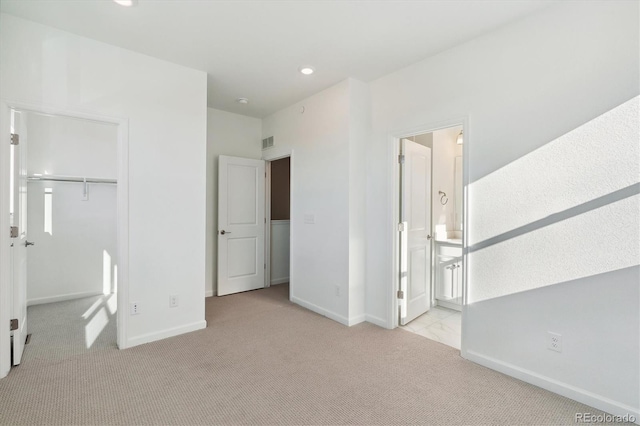 unfurnished bedroom with ensuite bath, a closet, and light colored carpet