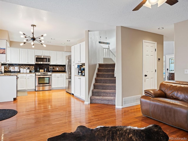 living room with ceiling fan with notable chandelier, light wood-type flooring, and a textured ceiling