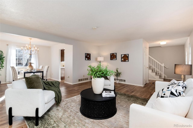 living area featuring visible vents, baseboards, stairway, wood finished floors, and a notable chandelier