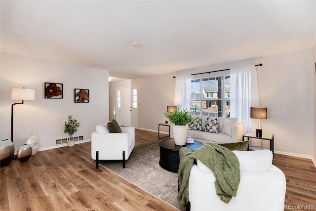 living area with a wealth of natural light, visible vents, baseboards, and wood finished floors