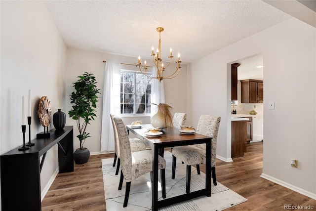 dining space with a notable chandelier, a textured ceiling, light wood-type flooring, and baseboards