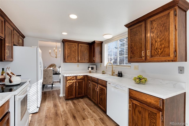 kitchen with light wood-style flooring, a sink, white appliances, an inviting chandelier, and light countertops